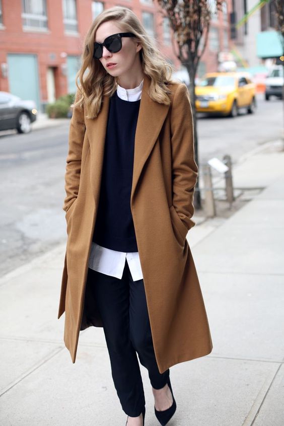 black pants, a black sweater over a white shirt, black suede shoes and a camel coat