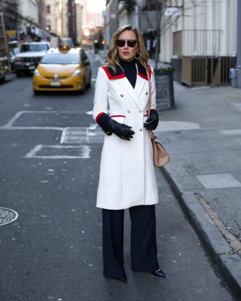 With navy blue trousers, black turtleneck, white coat and beige bag