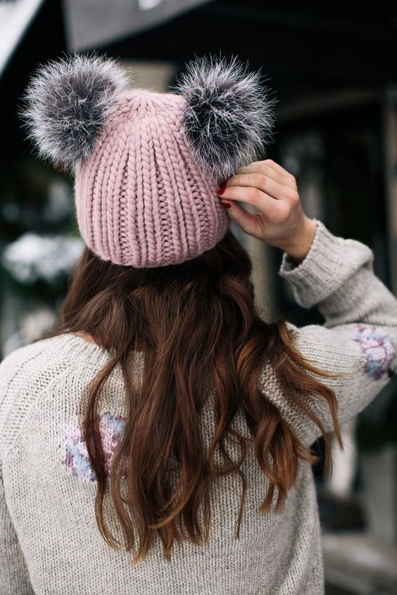 a chunky knit pink beanie with grey pompoms that imitate horns or ears