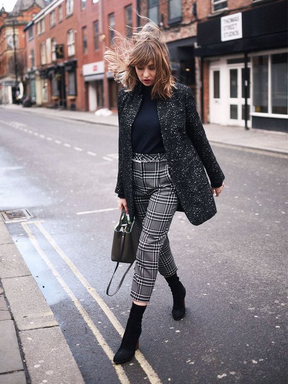 a black turtleneck, a long tweed jacket, plaid cropped pants and black sock boots
