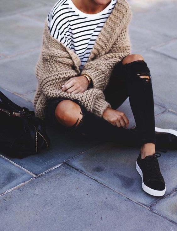 ripped black jeans, a striped top, black sneakers and a beige chunky knit cardigan