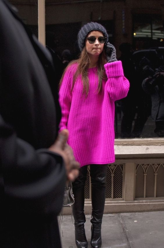 a neon pink chunky knit long sweater, black leather pants and boots and a black beanie