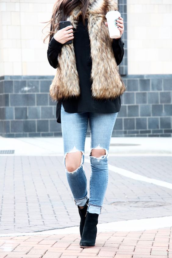 ripped jeans, a black sweater, black boots and a faux fur vest