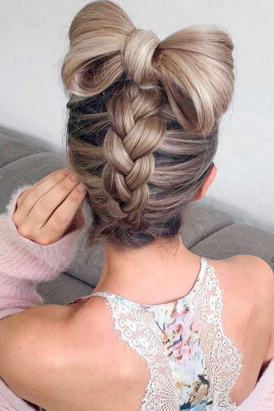 a fun braided updo with a large hair bow on top for a whimsy look