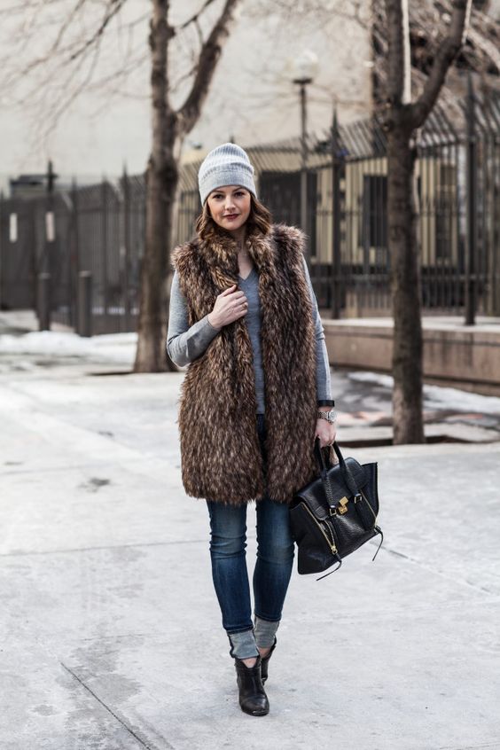 blue jeans, a grey top, black booties, a grey beanie and a long fur vest