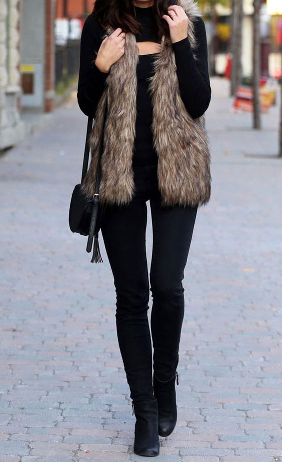 a total black look with jeans, boots, a cutout neckline sweater and a faux fur vest