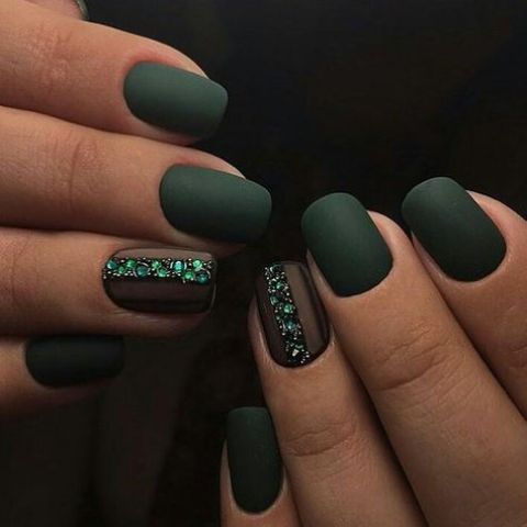 matte dark green nails with an accent nail lined up with emerald rhinestones