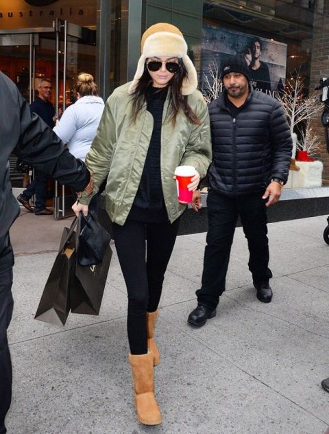 With black shirt, olive green jacket, black leggings and shearling hat