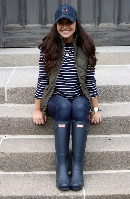 With striped shirt, olive green puffer vest, jeans and high boots