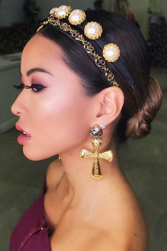 a low bun with a sleek top accented with a headband with chain and large pearls, with bold and statement earrings for the holidays