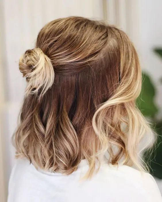 a medium hair half updo with a bump on top, a small bun and waves down plus face-framing hair