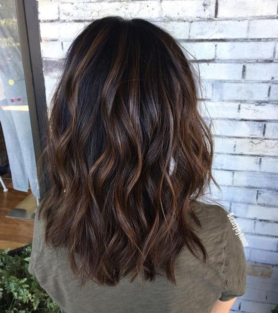 a black medium-length wavy hairstyle with caramel highlights and waves is a timeless idea to rock