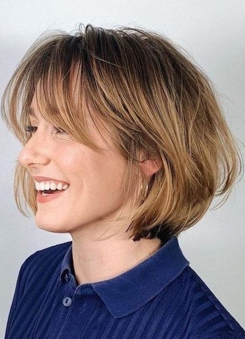 A chin length bob with honey blonde balayage and long curtain bangs, curved ends and a bit of volume