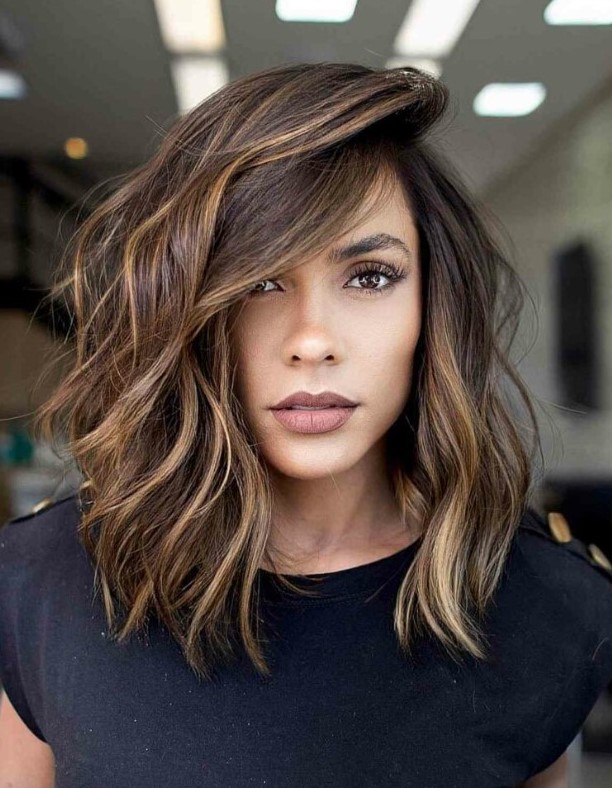A dimensional asymmetrical medium length haircut with side bangs and caramel highlights that bring even more dimension