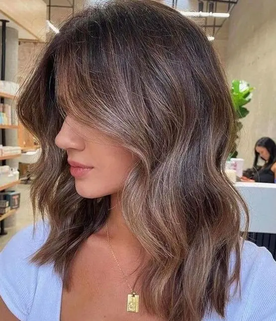 A lovely brunette medium length haircut with slight caramel contouring and highlights plus waves is very chic