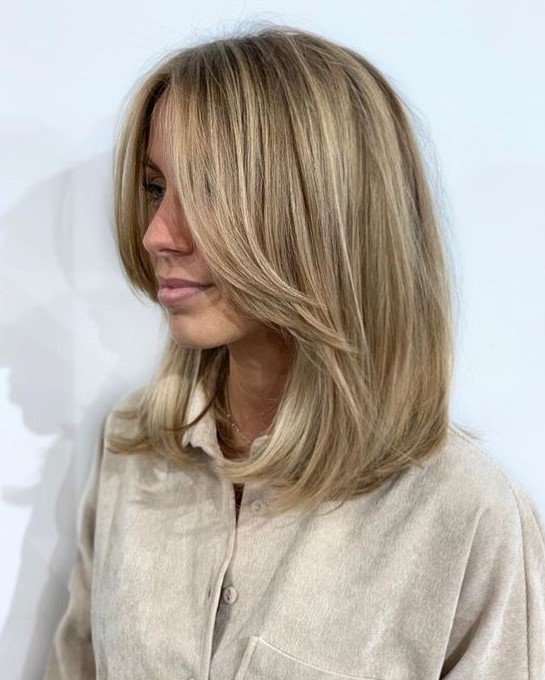 a medium-length blonde hairstyle with long curtain bangs and blonde balayage is a lovely and chic idea