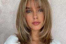 medium-length blonde hair with blonde balayage, layers and wispy bangs that beautifully frame the face