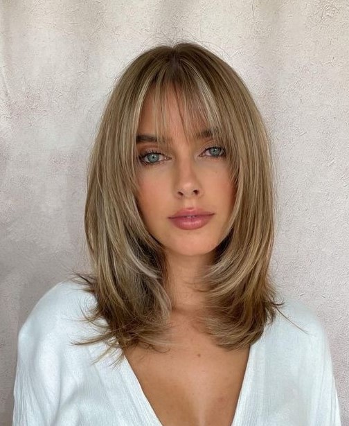 medium-length blonde hair with blonde balayage, layers and wispy bangs that beautifully frame the face