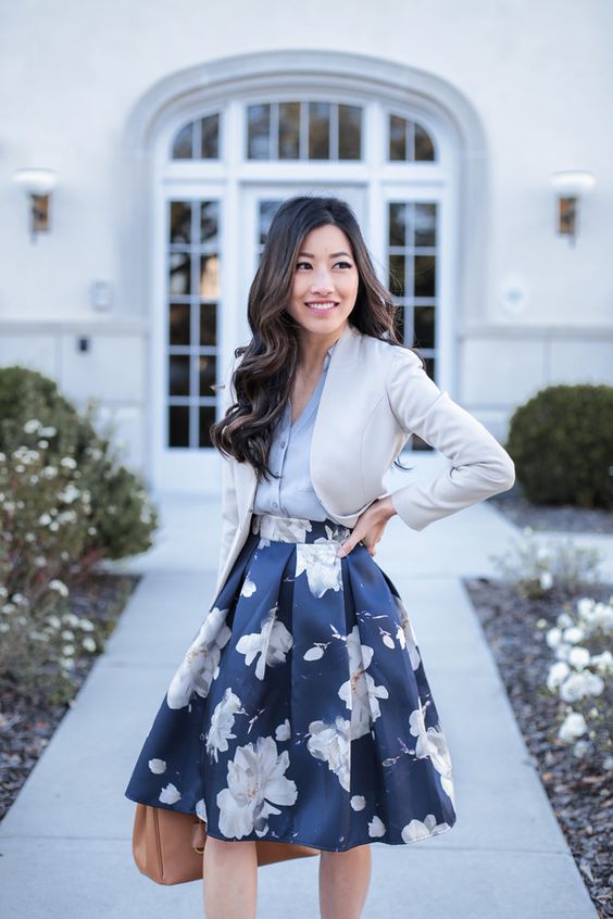 a full navy floral print skirt, a grey v neck shirt, a cropped creamy jacket and a brown bag