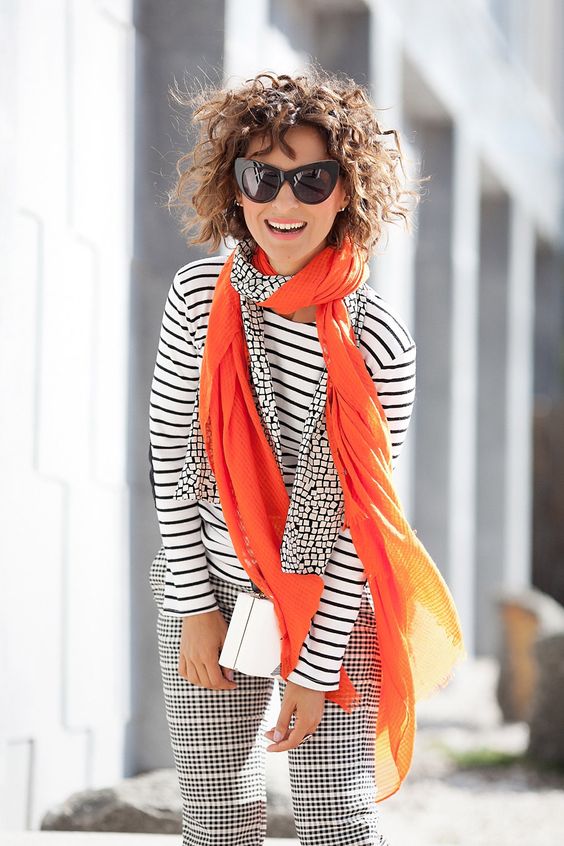 a striped black and white top, checked pants, an orange and printed scarf as an accent