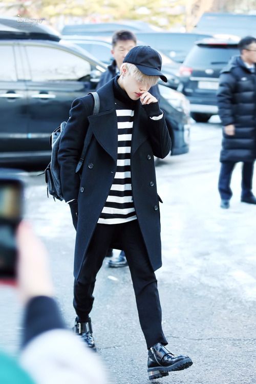 black pants, a striped top, a black coat, black boots and a baseball cap