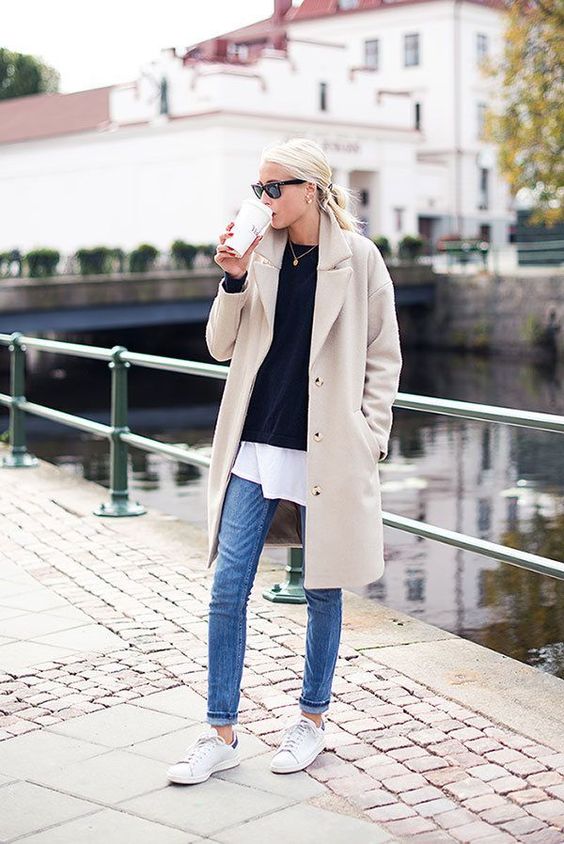 blue jeans, a white tee, a black pullover, white sneakers and a tan trench