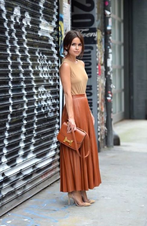 A nude top without sleeves, a cognac colored midi skirt, nude shoes and a cognac bag