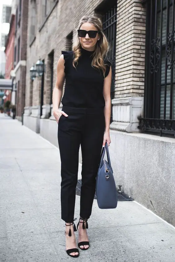 a black jumpsuit with a high neckline, ruffled sleeves, black tassel shoes and a blue bag for a casual business look