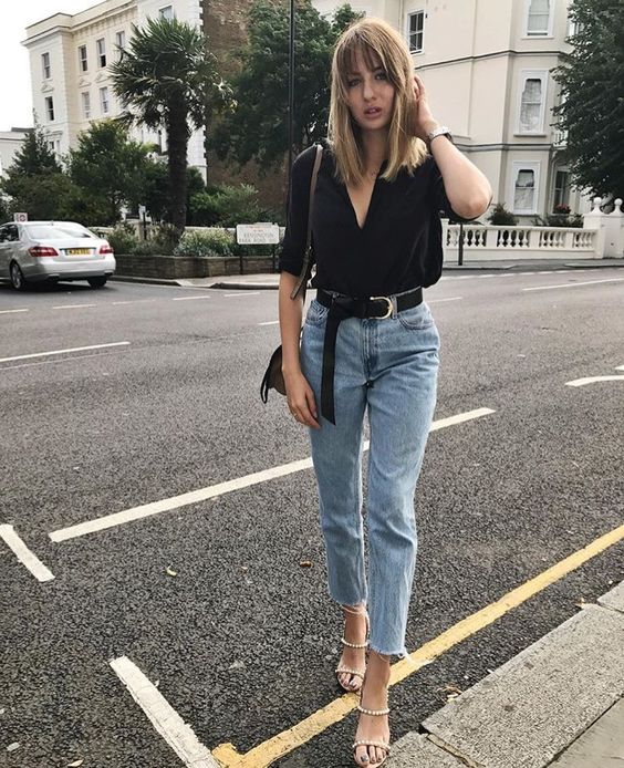 a black blouse, light blue high waisted raw hem jeans and metallic strappy shoes
