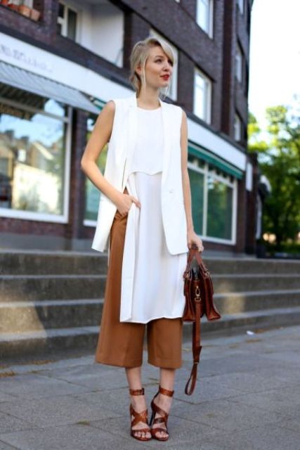 brown culottes, a long white top with a slit, a long white vest, brown strappy shoes and a bag