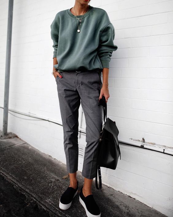 an olive green sweatshirt, cropped grey trousers, black slipons and a black backpack