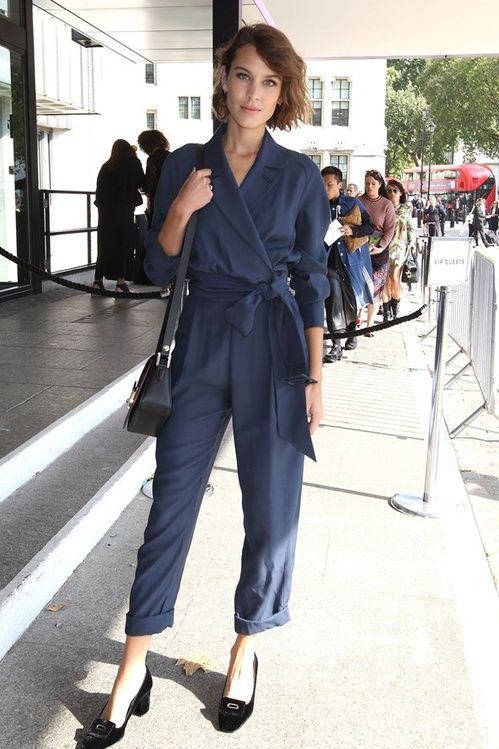 a navy jumpsuit with a sash, long sleeves, black retro shoes and a black bag for a formal look