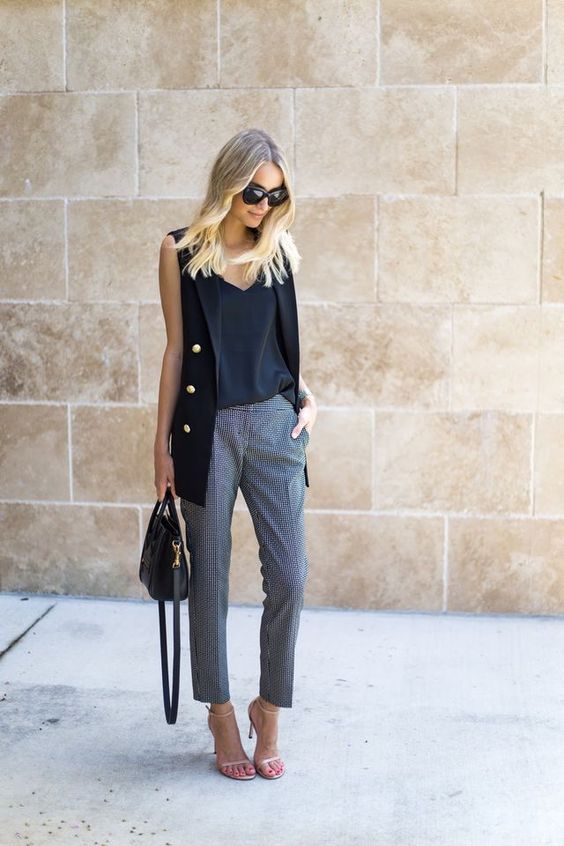 a black top and long vest with gold buttons and printed cropped pants, nude shoes and a black bag