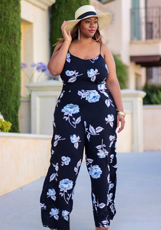 a navy floral print jumpsuit on spaghetti straps, brown heels and a hat for a vacation look
