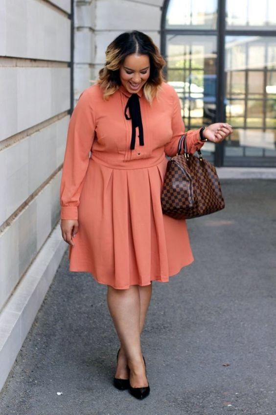 a bright orange knee dress with a pleated skirt and a black ribbon bow, a checked bag and black heels for a bold work look