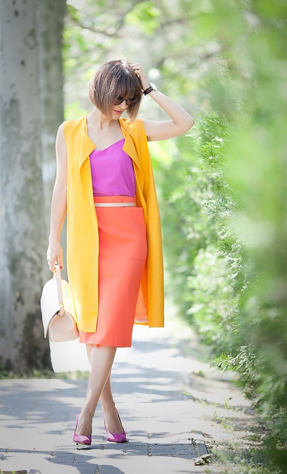a hot pink top and shoes, an orange midi skirt, a long yellow vest and a creamy bag