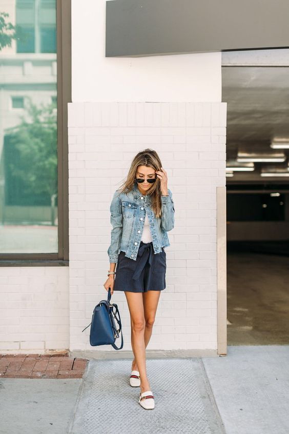 a white top, navy denim shorts, a blue denim jacket, a navy backpack and neutral moccasins