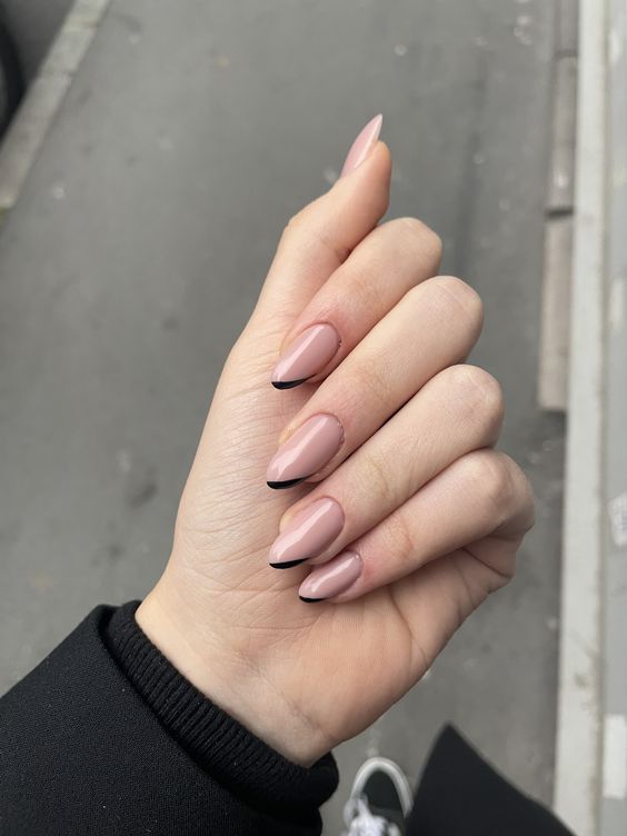 a modern take on French nails done in blush and black, with black tips placed diagonally and on one side only