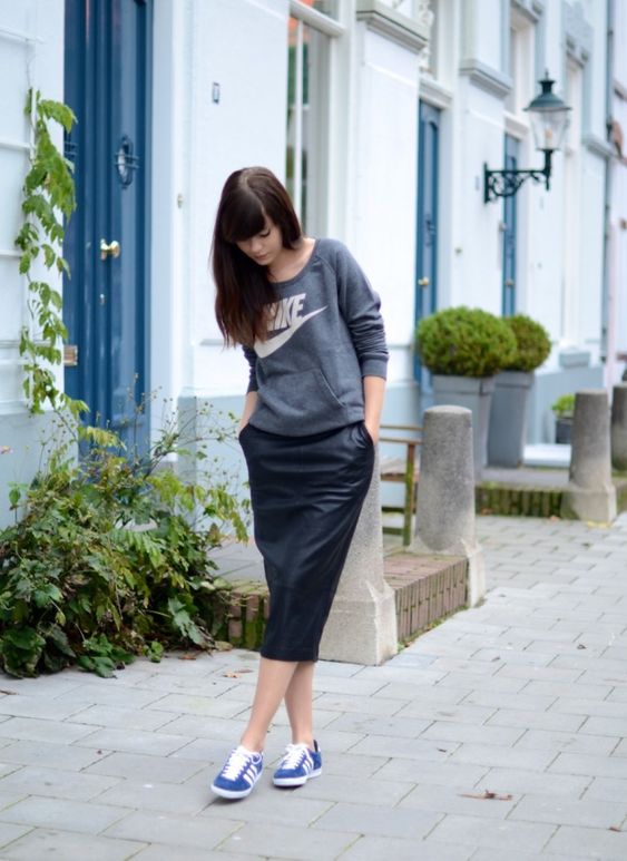 a sport chic look with a grey sweatshirt, a black leather midi and blue sneakers