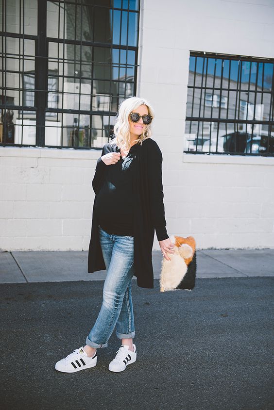 distressed jeans, a black t-shirt, white sneakers, a black long cardigan and a faux fur clutch
