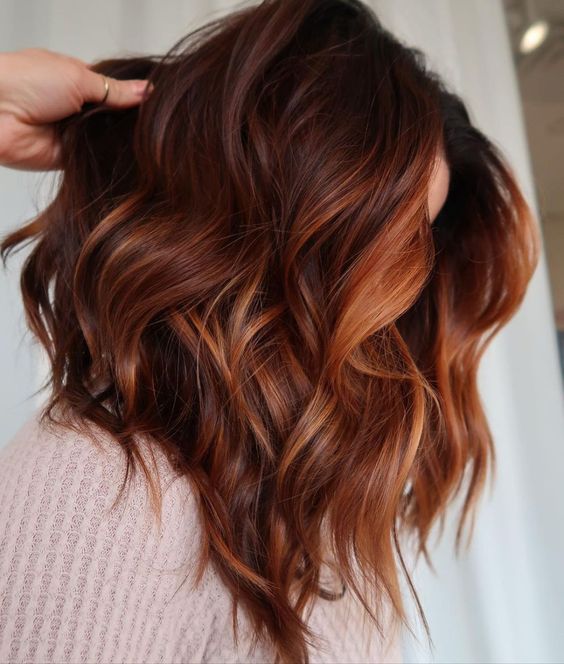 Medium length auburn hair with orange and copper highlights, with waves and volume, is a stunning solution that wows