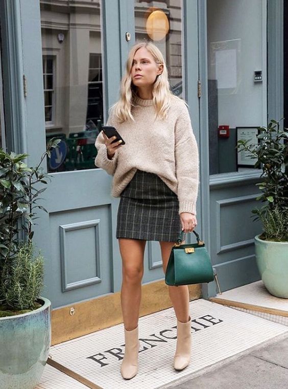 a blush oversized sweater tucked in a dark plaid mini skirt, creamy boots, an emerald bag