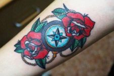 Compass and red flowers tattoo on the forearm