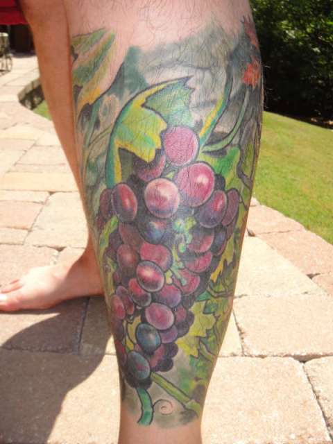 Green leaves and grape tattoo on the leg
