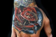 Red rose, blue water and ship wheel tattoo on the hand