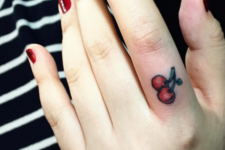 small cherry tattoo on woman’s finger