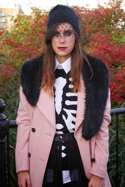 With pink coat with black fur, white shirt, printed sweater and skirt