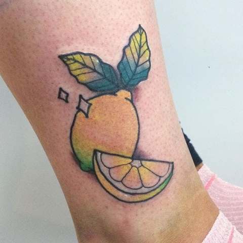 Yellow lemon and green leaves tattoo on the leg