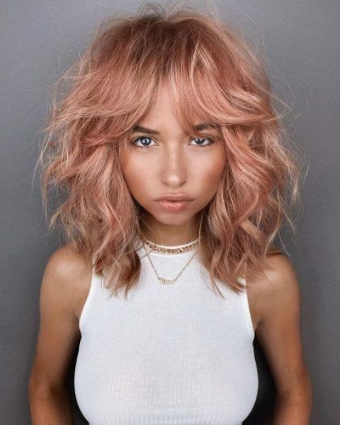 Medium length strawberry blonde messy and shaggy hair with a lot of volume and bottleneck bangs