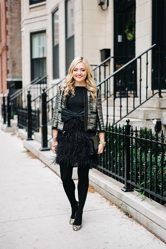 a black dress with a large bow and a feather skirt, black tights, embellished shoes and a gild blazer
